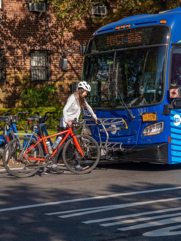 A person in a bike helmet walking their bicycle up to a bus with a bike rack